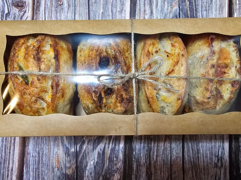 Four sourdough loaves in a windowed kraft box tied with twine, on dark planks