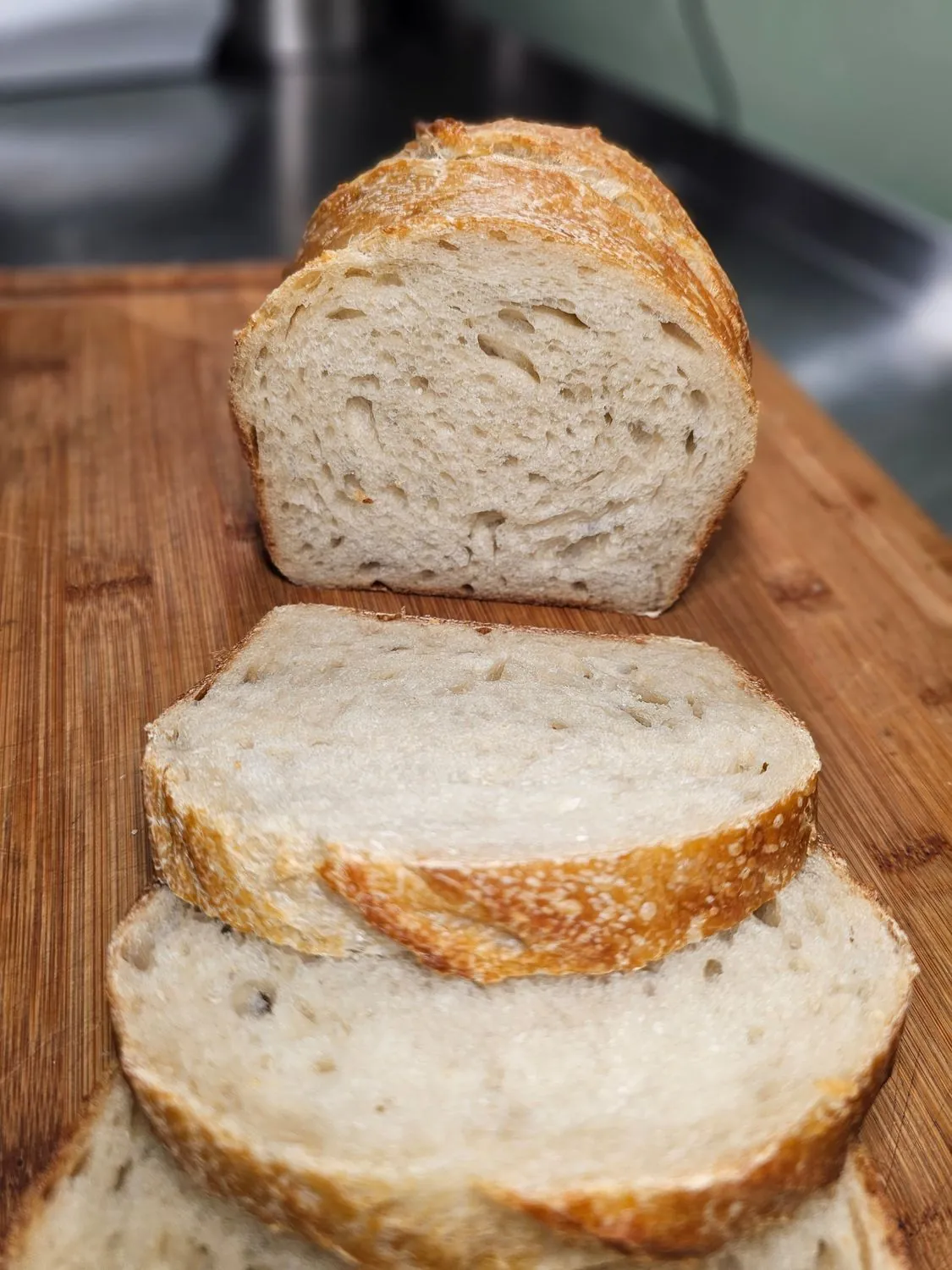 A sourdough sandwich loaf sliced on a bamboo board, its open crumb facing out